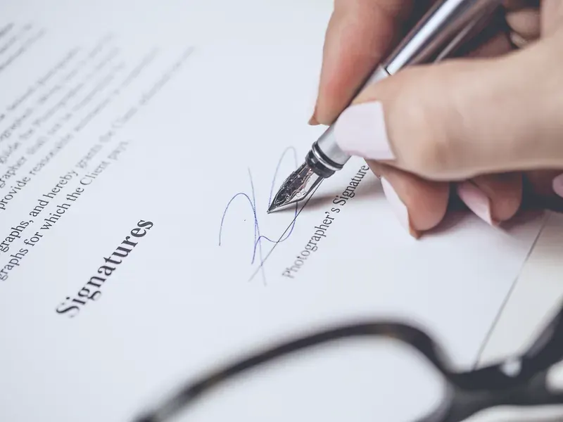 Main signant un document au stylo plume, lunettes posées au premier plan