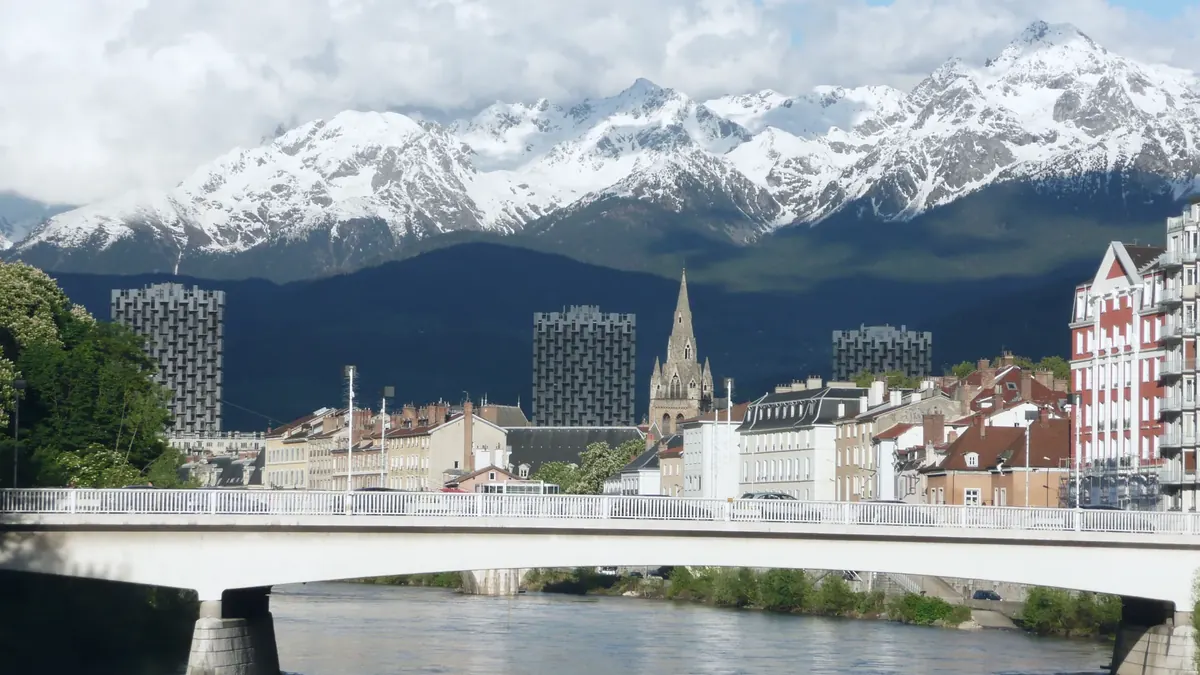 grenoble-isere-alpes Grenoble depuis les quais de l'Isère : pont, toits, clocher et tours, devant le massif de Belledonne enneigé