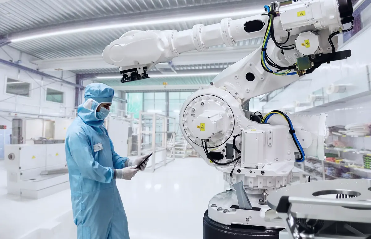Technicien en combinaison de salle blanche consultant une tablette à côté d'un robot industriel six axes